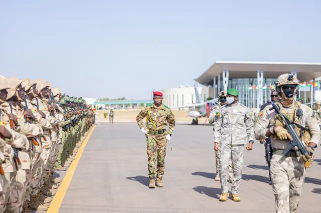 Assimi Goita, le président de la Transition au Mali en tenue militaire et un béret vert avec un cache-nez passe en revue les troupes.