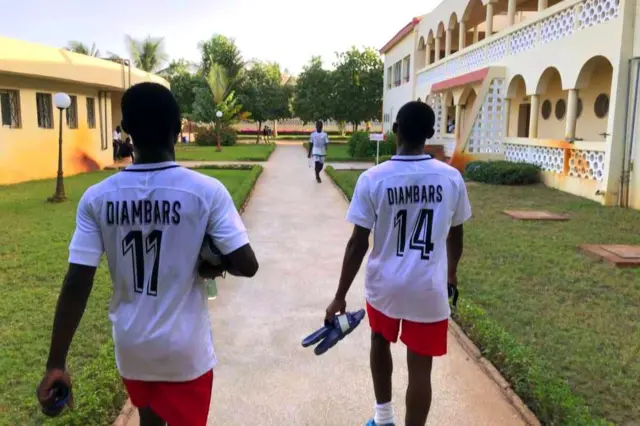 Deux joueurs vêtus de maillot blanc et short rouges marchent en direction du terrain.