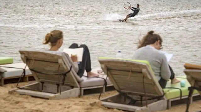 Deux vacanciers européens profitent de chaises longues au bord de la plage du Sahara occidental tandis qu'un autre s'adonne au kitesurf dans les eaux atlantiques