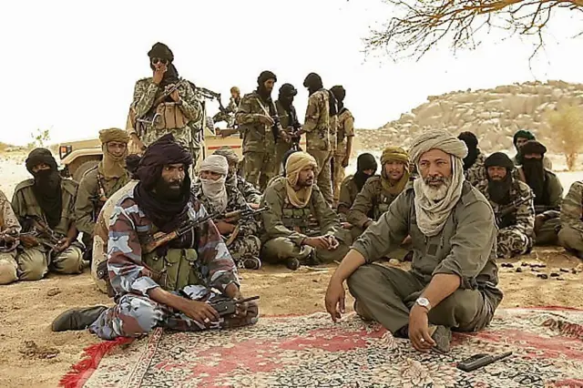 Combattants touaregs discutant sous un arbre dans une zone désertique